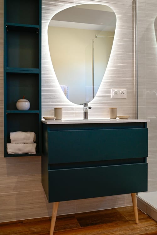Modern bathroom vanity with teal cabinets, illuminated mirror, and white countertop at Pavillon Des Millesimes hotel
