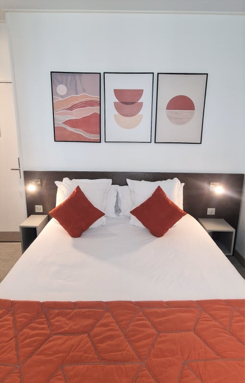 Camera d'hotel moderna all'Hôtel De La Fontaine a Nizza con letto bianco, cuscini rossi e arte murale astratta contemporanea