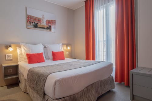 Camera moderna presso l'Hôtel De La Fontaine a Nizza con letto queen, accenti rossi, vista sulla città e porte-finestre