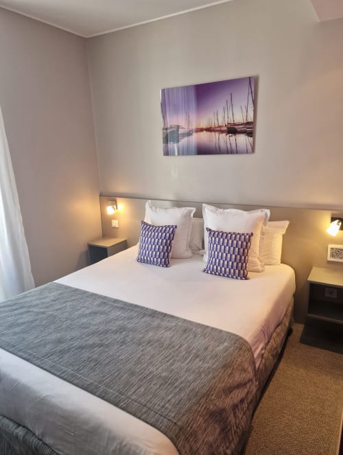Camera d'albergo moderna presso l'Hôtel De La Fontaine a Nizza con letto matrimoniale, cuscini viola, illuminazione calda e vela