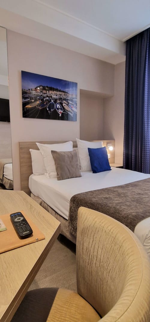 Camera moderna dell'Hôtel De La Fontaine a Nizza con letto queen, scrivania, opera d'arte marina e tende blu scuro