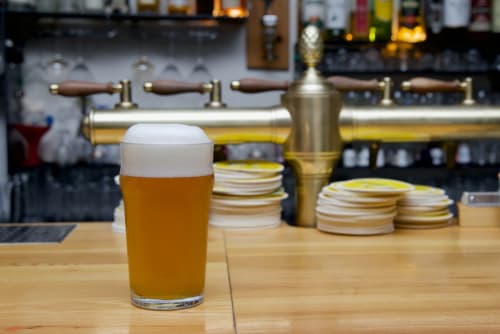 Golden beer with foam head on wooden bar at Au Gite d'Isigny, Isigny-sur-Mer, with tap handles and coasters visible