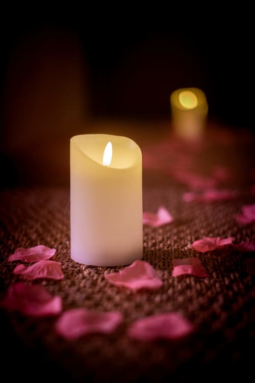 Glowing LED candle surrounded by pink petals on brown fabric at Villa Eden Bleu, Biscarrosse