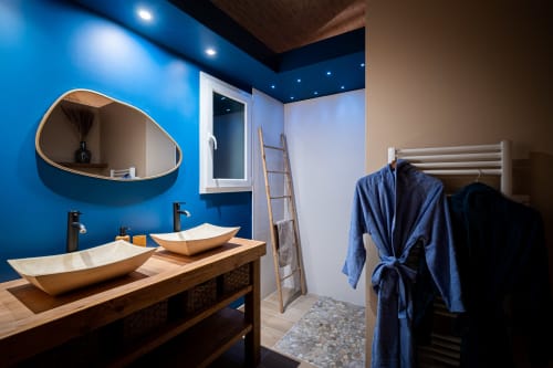 Modern bathroom at Villa Eden Bleu with blue accent wall, dual vessel sinks, wooden vanity, and heated towel rack