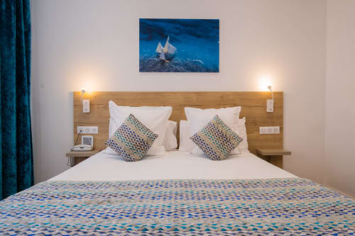 Modern hotel bedroom at Hôtel De La Fontaine in Nice with wooden headboard, patterned bedding, and ocean sailboat artwork