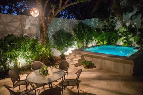 Patio de villa en Cancún iluminado de noche con esfera luminosa, mesa de comedor, tumbonas, plantas tropicales e iluminación ambiente