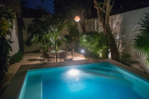 Piscina privada iluminada por la noche en villa tropical con patio, palmeras y área de comedor en Cozy House Downtown Cancun