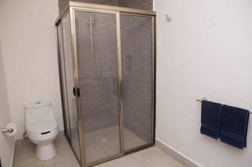 Baño moderno con ducha tipo vestidor, inodoro y toallero en la villa Cozy House Centro de Cancún