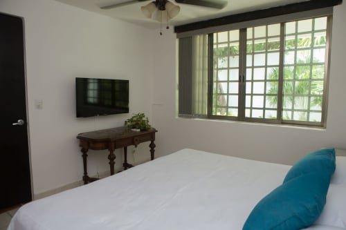 Dormitorio luminoso de villa con cama blanca, TV plana, escritorio de madera y grandes ventanales con vistas a piscina en Cozy House Downtown