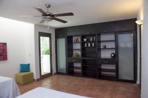 Recámara de villa moderna en Cancún con estanterías empotradas negras, ventilador de techo, piso de terracota y acceso a terraza exterior