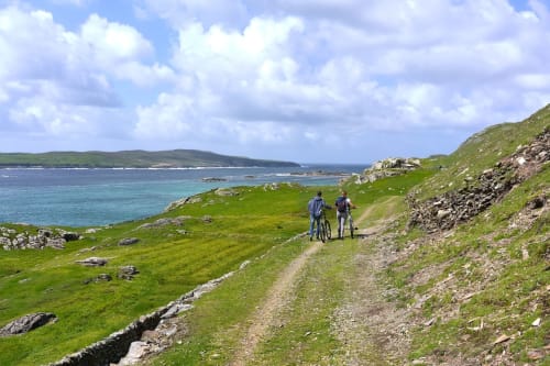 Two hikers on coastal trail overlooking turquoise waters near Seabrook Lodge, Clifden, Galway