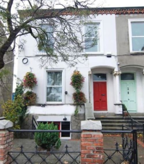Eglinton Road Bray BnB exterior with white facade, red and green doors, hanging baskets, and bare tree branches overhead