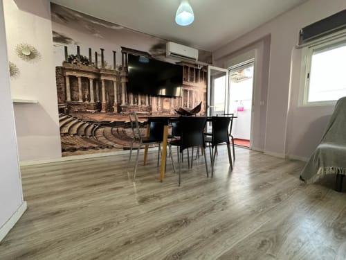 Apartamento moderno en Mérida con suelos de madera, comedor, televisor, mural de anfiteatro romano y vistas a la ciudad.