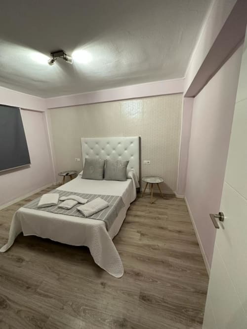 Moderna habitación del apartamento Gestyp-AT en Mérida con cama tapizada blanca, piso de madera y mobiliario contemporáneo