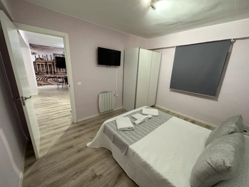 Moderno dormitorio de apartamento en Mérida con cama, TV, escritorio y vista a la ciudad desde la puerta abierta hacia la sala de estar