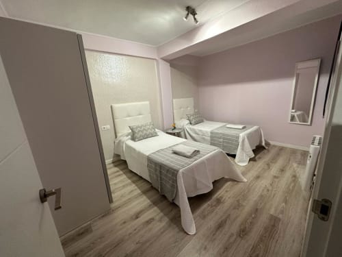Dormitorio doble en apartamento Gestyp-AT, Mérida con camas, cabeceros blancos, suelos de madera y vistas a la ciudad