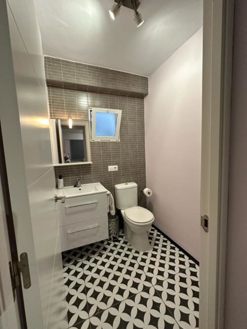 Baño moderno del apartamento Gestyp-AT en Mérida con piso de azulejos geométricos, pared de azulejos grises, lavamanos, inodoro y ventana tipo tragaluz