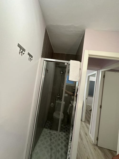 Baño moderno con ducha de cristal, azulejos oscuros en el interior, paredes blancas, toallero y diseño abierto en apartamento de Mérida