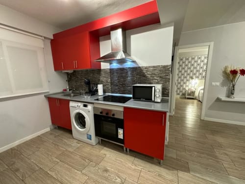 Moderna cocina roja con electrodomésticos de acero inoxidable y salpicadero oscuro en apartamento de Mérida