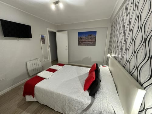 Dormitorio moderno en Mérida con cama blanca, acentos rojos, paredes empapeladas, TV y cuadro con vista de la ciudad