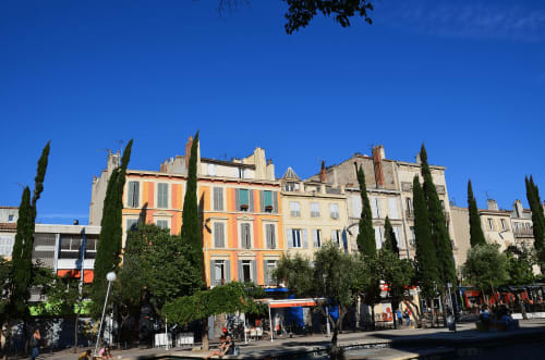 Bâtiments colorés français avec cyprès et boutiques au rez-de-chaussée à Belvès-de-Castillon