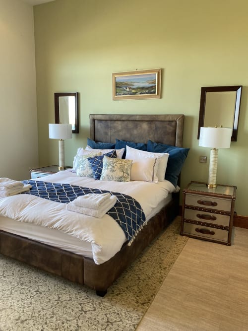 Seabrook Lodge bedroom in Clifden with gray upholstered bed, blue bedding, twin lamps, and pale yellow walls