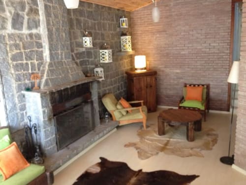 Aconchegante sala de estar da vila Paraíso nas Montanhas com lareira, paredes de pedra, móveis confortáveis e vistas para as montanhas em Campos do