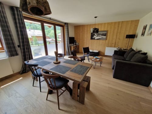 Modern open-plan living area at Serre Chevalier Cristal Lodge with dining table, black sofa, wood-paneled walls, and mountain