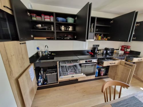 Modern kitchen with black countertops, wood cabinets, and open upper storage at Serre Chevalier Cristal Lodge in