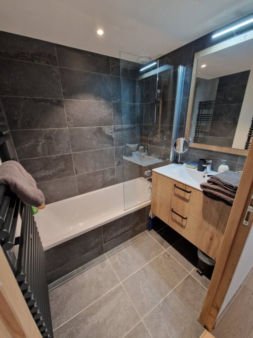 Modern bathroom at Serre Chevalier Cristal Lodge with dark tile, glass shower enclosure, wooden vanity and heated towel rack