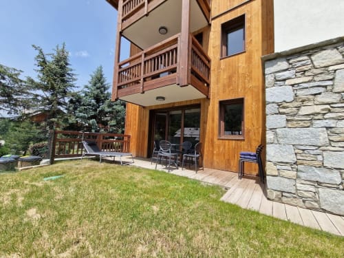 Modern wooden lodge with stone accents, tiered decks, and manicured lawn at Serre Chevalier Cristal Lodge