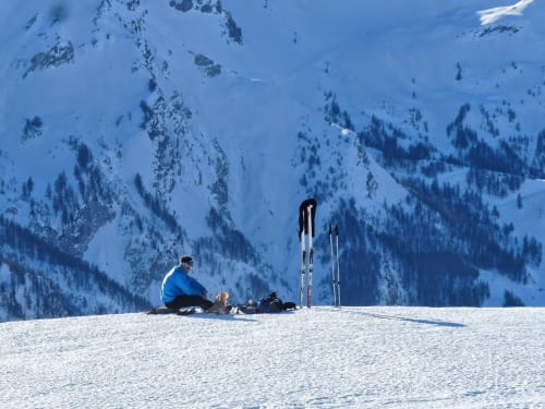Sciatore che si riposa sul pendio innevato con vista sulla valle di montagna presso il Serre Chevalier Cristal Lodge, Saint-Chaffrey