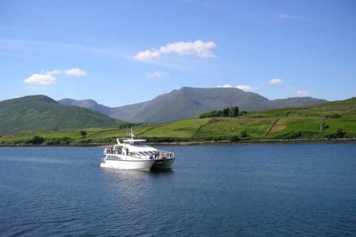 Tour boat on blue waters near Seabrook Lodge, Clifden, with green mountains and Irish coastline backdrop
