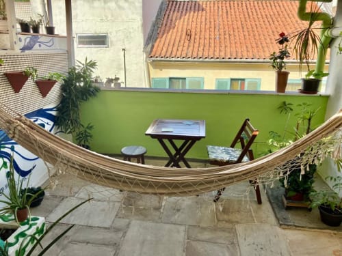 Terraço da varanda do Hostel New Ipanema com rede, área de estar, paredes verdes e vista do jardim urbano no Rio de Janeiro