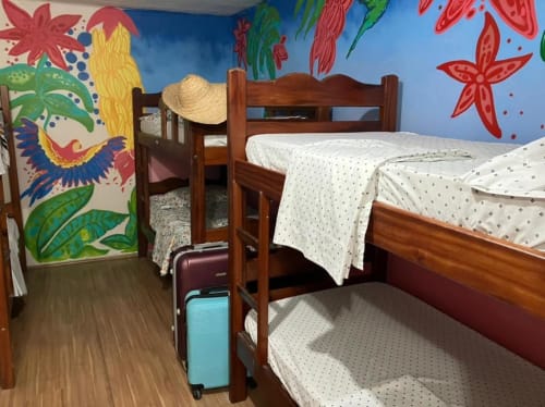 Quarto colorido no Hostel New Ipanema no Rio de Janeiro com beliches de madeira, arte tropical na parede e área compartilhada