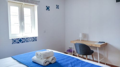 Quarto Santo António na casa de hóspedes Ó da Casa em Peniche com cama azul, secretária e vista para a cidade