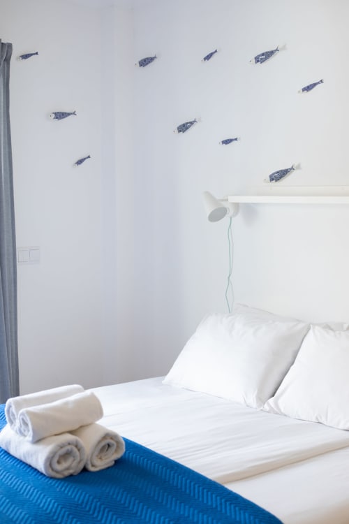 Quarto Sardinha em Ó da Casa em Peniche com roupa de cama azul e branca, toalhas enroladas e adesivos de peixes azuis acima da cama