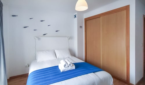 Quarto aconchegante em Ó da Casa B&B em Peniche com destaque azul, roupa de cama branca, guarda-roupa de madeira e decoração náutica