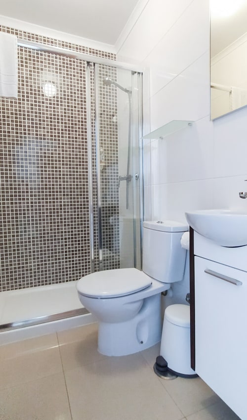 Casa de banho moderna no quarto Sardinha da pensão Ó da Casa, Peniche com chuveiro, sanita, lavatório e piso em azulejo bege
