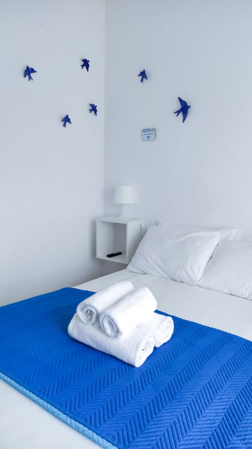 Aconchegante quarto em Ó da Casa, Peniche com cama azul, almofadas brancas, toalhas enroladas e decoração de parede com pássaros azuis