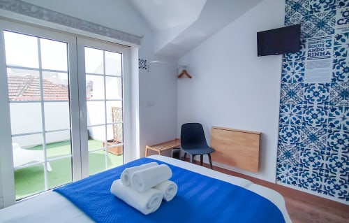 Quarto luminoso na pousada Ó da Casa em Peniche com roupas de cama azuis, toalhas brancas, parede com azulejos portugueses e varanda