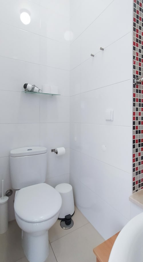 Banheiro branco moderno com vaso sanitário, pia e chuveiro em quarto do hotel boutique Ó da Casa em Peniche, Portugal