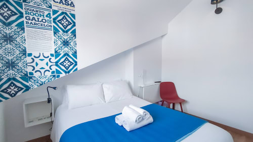 Quarto aconchegante na pousada Ó da Casa em Peniche com arte de parede azul, cama branca, toalhas enroladas e cadeira vermelha