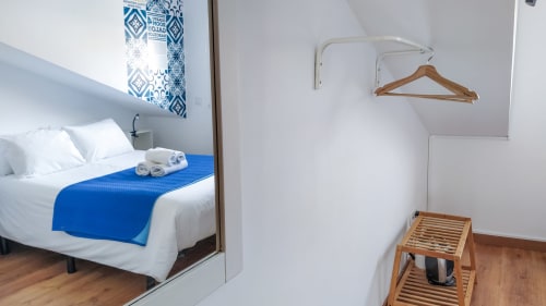 Quarto moderno em Ó da Casa em Peniche com cama em destaque azul, prateleiras de madeira e cabideiro