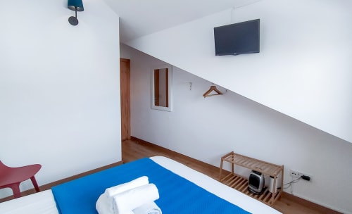 Quarto Galo de Barcelos na Ó da Casa BnB em Peniche com cama azul, TV de tela plana, piso de madeira e teto inclinado