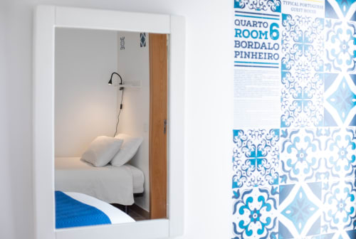 Quarto 6 Bordalo na pousada Ó da Casa em Peniche, Portugal, com cama bem arrumada de lençol branco e espaço de leitura
