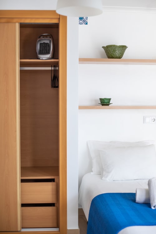Quarto em Ó da Casa em Peniche com guarda-roupa de madeira, prateleiras flutuantes com plantas e cama com manta azul