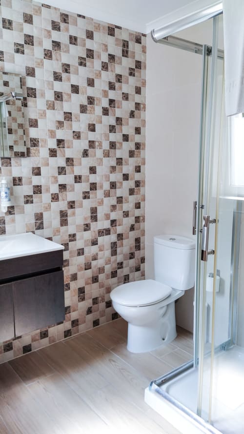 Banheiro moderno com azulejos xadrez marrom e branco, vaso sanitário branco, móvel suspenso escuro e chuveiro em vidro em Ó da Casa