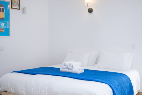 Quarto moderno e limpo em Ó da Casa B&B em Peniche com roupas de cama brancas, manta azul, toalhas enroladas e vista para o jardim