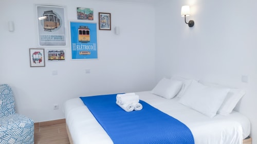 Quarto luminoso no Ó da Casa B&B em Peniche com roupa de cama branca, passadeira azul e decoração com arte vintage de bonde
